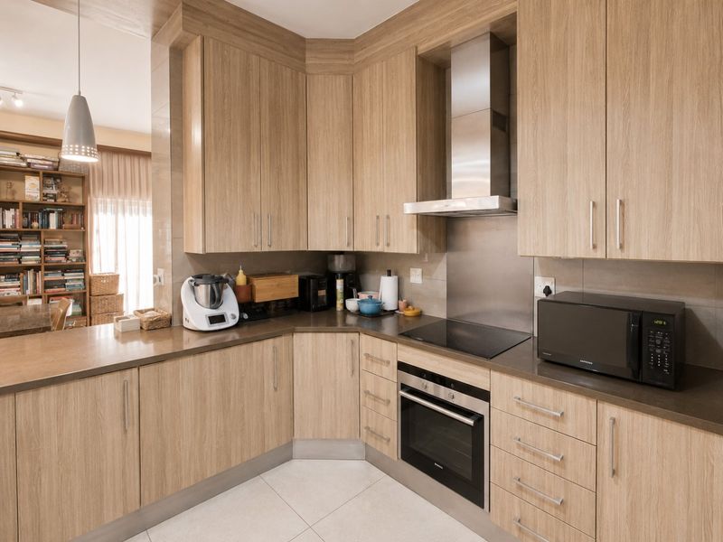 Modern kitchen featuring light wood-grain cabinetry, stone countertops, integrated stainless steel appliances, and a sleek electric cooktop with a matching extractor fan.