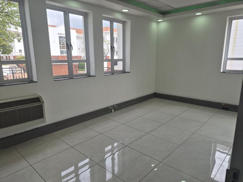 A bright, empty office space featuring polished tiled flooring, recessed ceiling lighting, and an integrated air conditioning unit with large windows.