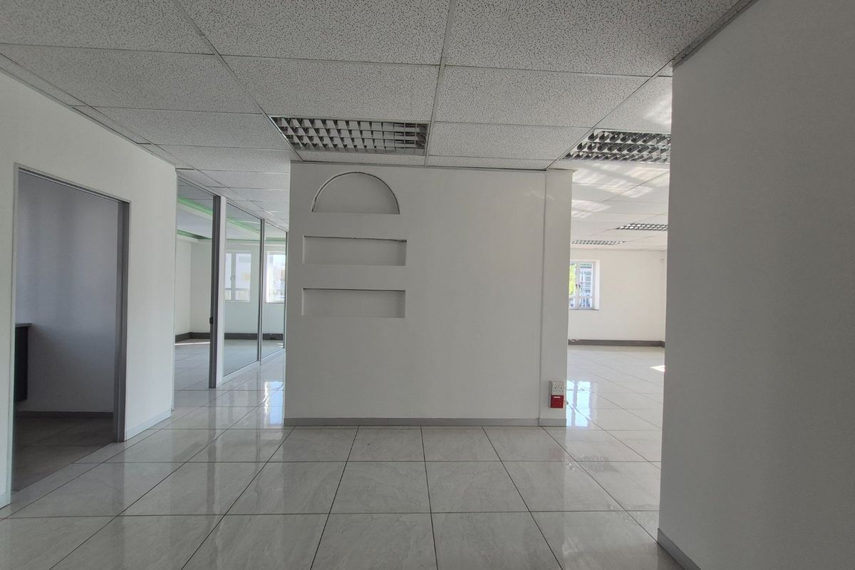 An open-plan commercial office space featuring tiled flooring, suspended ceilings with recessed lighting, and glass partition walls, offering a clean and professional environment.