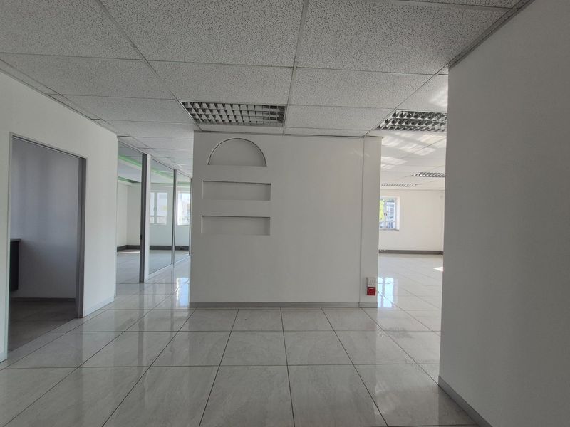 An open-plan commercial office space featuring tiled flooring, suspended ceilings with recessed lighting, and glass partition walls, offering a clean and professional environment.