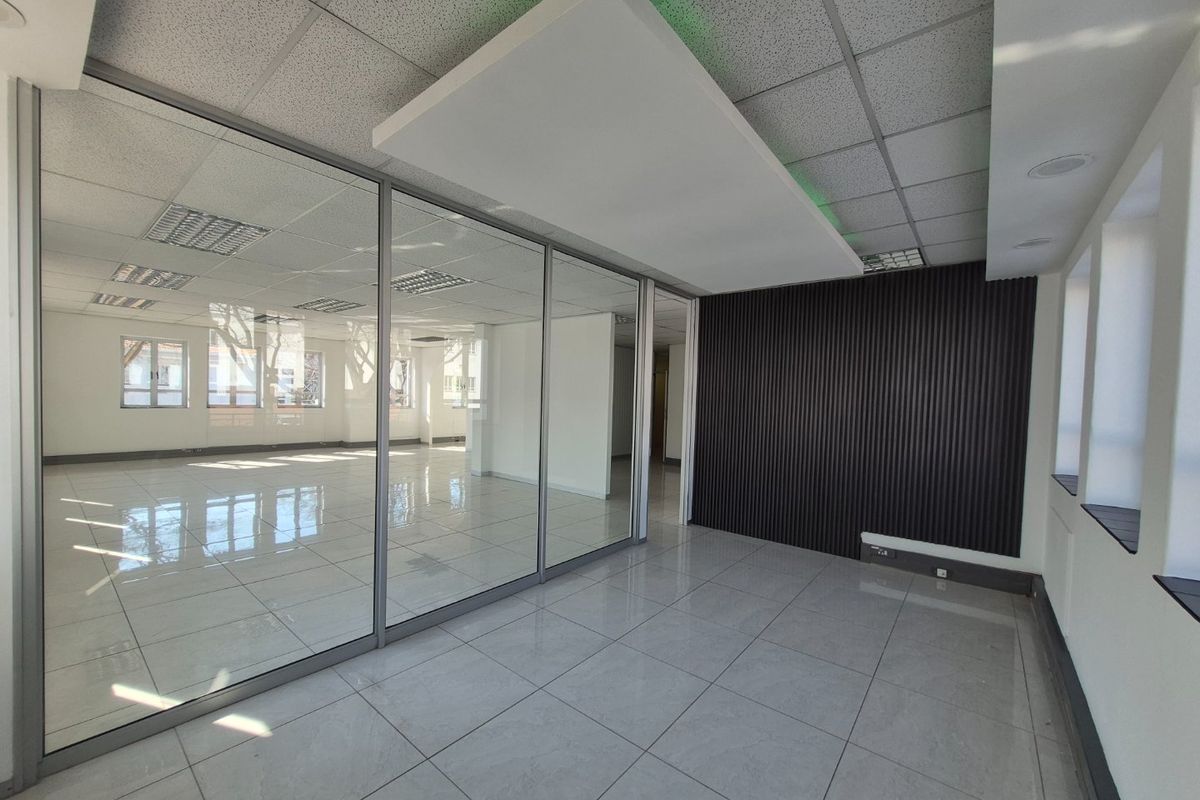 Modern commercial office space featuring glass partitions, sleek tiled flooring, a contemporary slatted feature wall, and a suspended ceiling with integrated lighting.