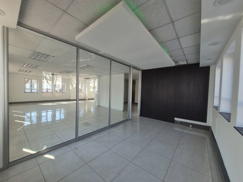 Modern commercial office space featuring glass partitions, sleek tiled flooring, a contemporary slatted feature wall, and a suspended ceiling with integrated lighting.