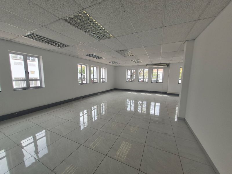 A bright, open-plan commercial office space featuring polished tiled flooring, suspended ceilings with recessed lighting, and multiple windows providing natural light.