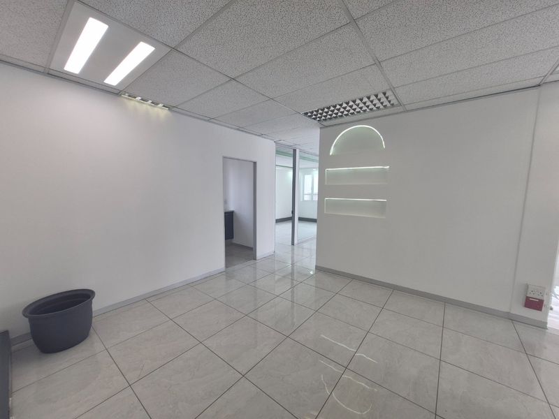 A bright, vacant commercial office space featuring polished ceramic floor tiles, a modern suspended ceiling with LED lighting, and a decorative illuminated wall niche.