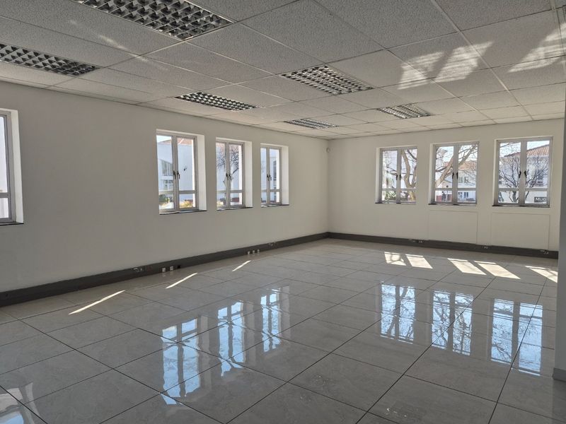 A bright, vacant commercial office space featuring polished tiled flooring, a suspended ceiling with recessed lighting, and multiple windows providing ample natural light.