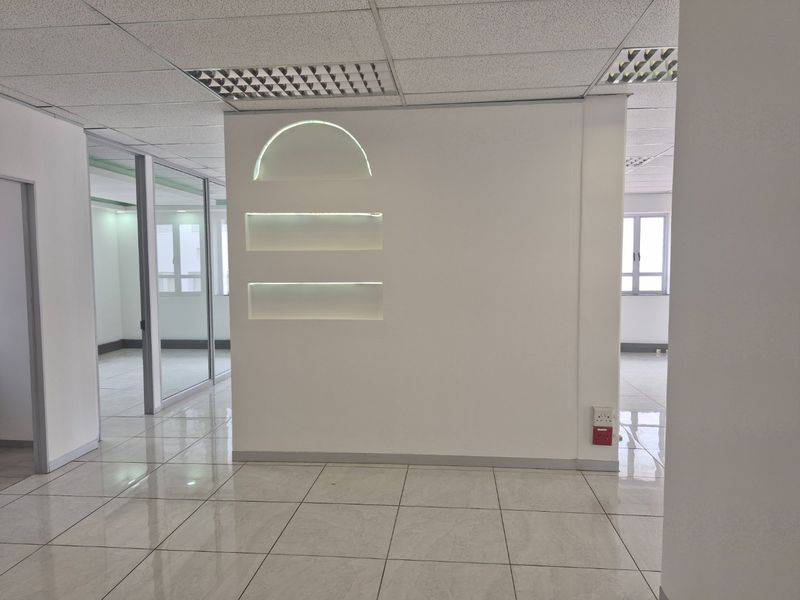 A bright, modern commercial office space featuring polished tile flooring, glass partitions, and a central feature wall with integrated recessed lighting niches.