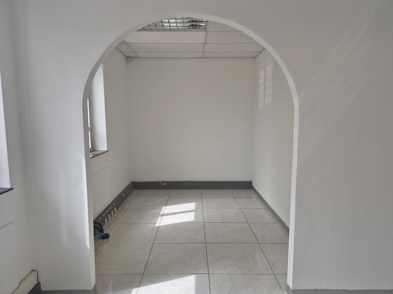 A vacant office space featuring an arched entrance, tiled flooring, and a suspended ceiling with integrated electrical trunking.