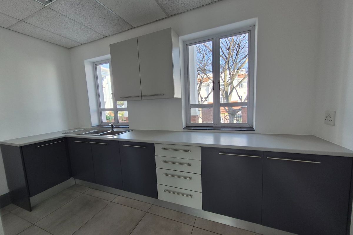 A clean, modern commercial kitchen space featuring dark and light grey cabinetry, ample counter space, stainless steel sink, and neutral tiled flooring.