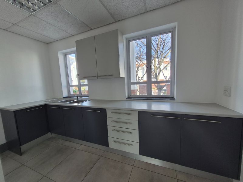 A clean, modern commercial kitchen space featuring dark and light grey cabinetry, ample counter space, stainless steel sink, and neutral tiled flooring.