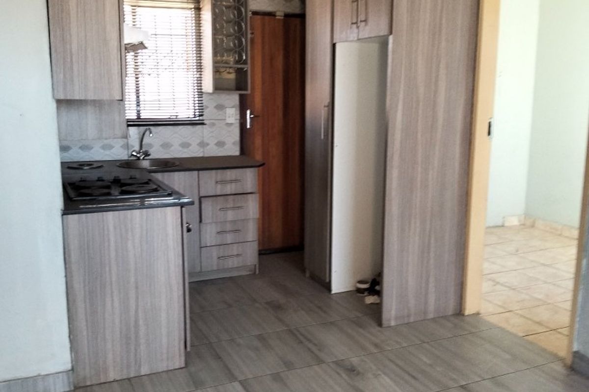 A compact kitchen featuring wood-look cabinetry, built-in hob, sink, and modern tiled flooring, offering a functional space ready for personalization.