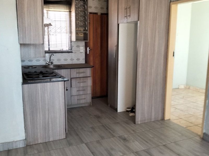 A compact kitchen featuring wood-look cabinetry, built-in hob, sink, and modern tiled flooring, offering a functional space ready for personalization.