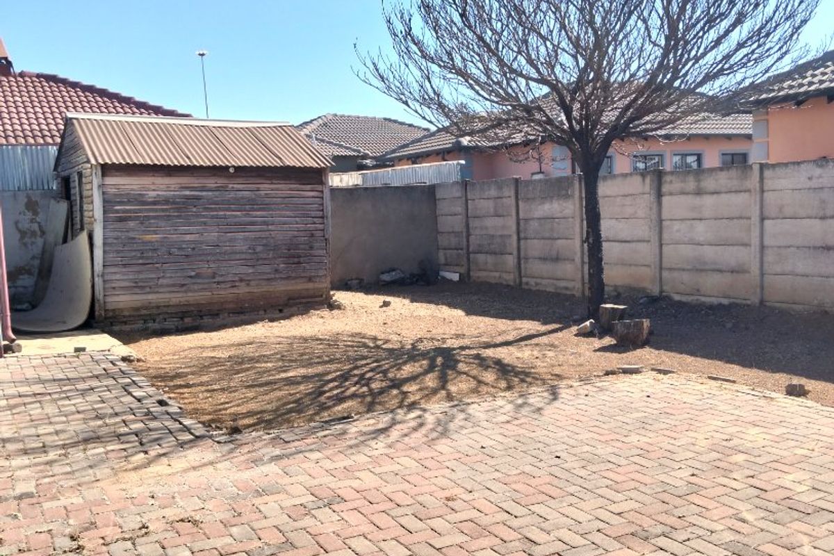 Rear exterior area featuring paved ground, a precast concrete boundary wall, and a weathered wooden storage shed in the garden.
