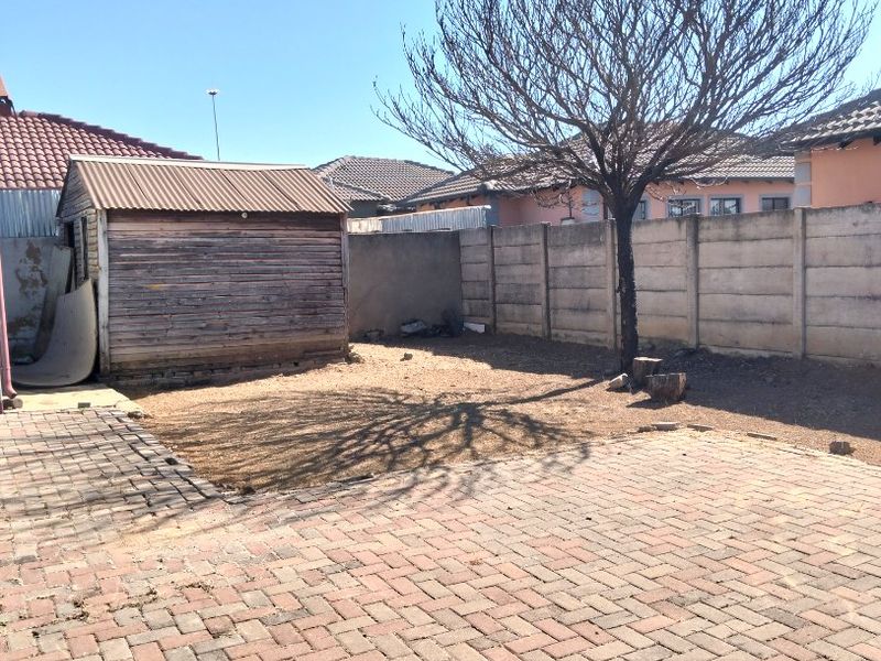 Rear exterior area featuring paved ground, a precast concrete boundary wall, and a weathered wooden storage shed in the garden.