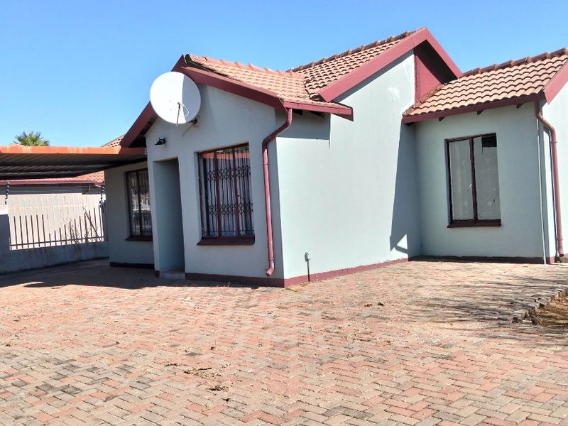 Front elevation of a single-story house featuring a tiled roof, paved driveway, carport, and security bars on windows.
