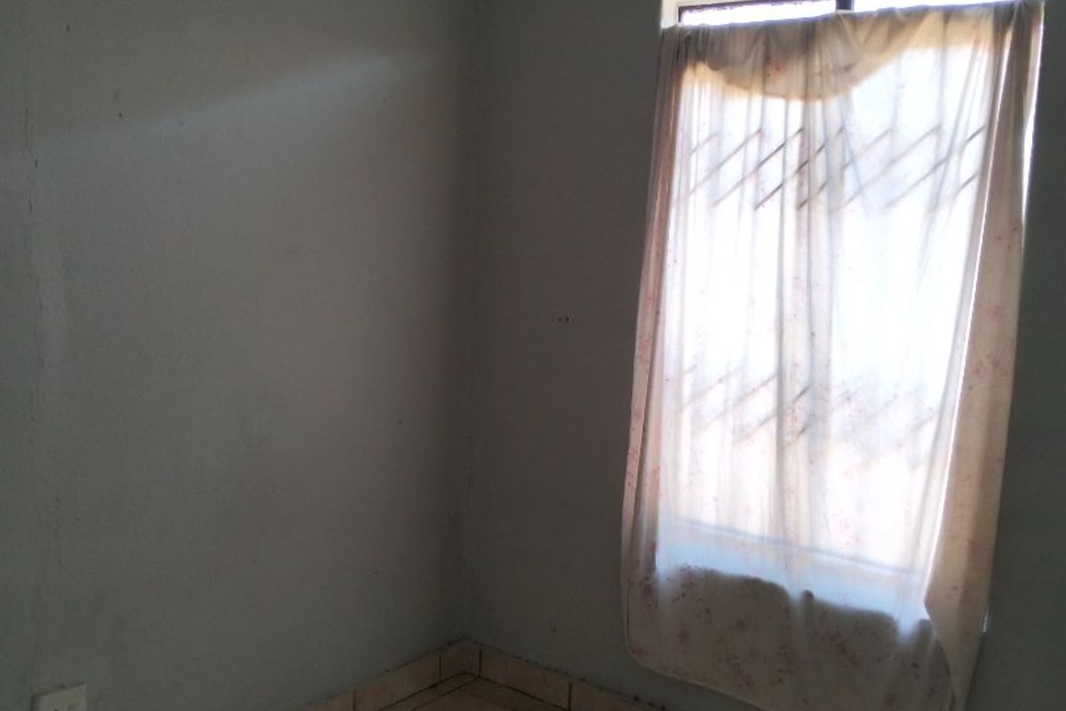 An empty bedroom featuring tiled flooring, a window with a security gate, and neutral wall finishes.