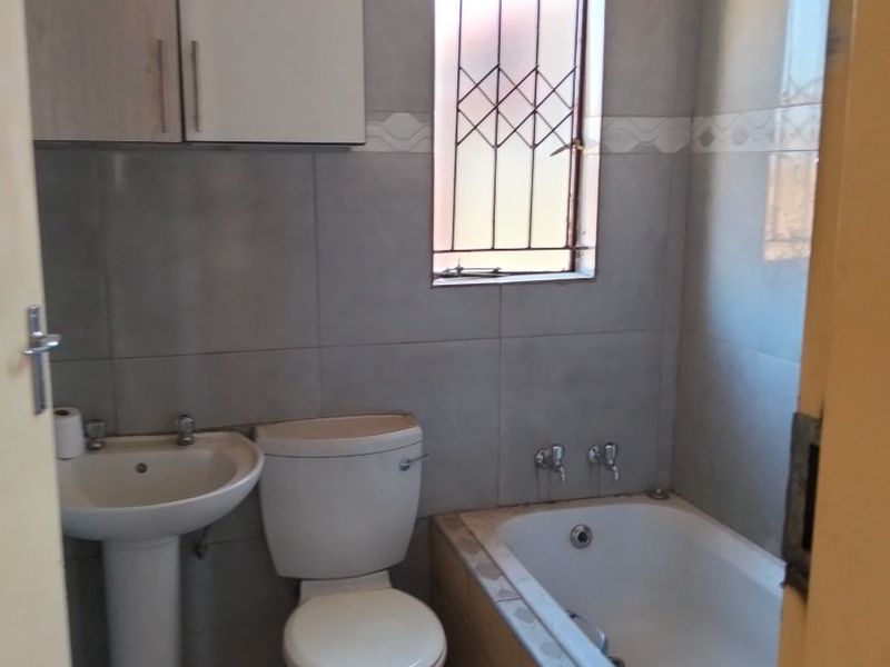 A functional bathroom featuring a pedestal basin, toilet, and bathtub with tiled finishes and wall-mounted storage cabinetry.