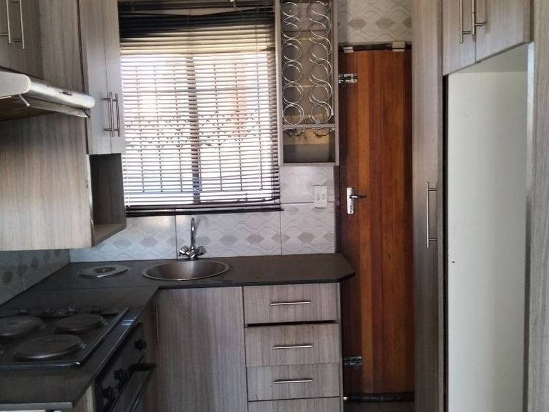A functional kitchen featuring wood-look cabinetry, dark countertops, built-in oven and hob, and tiled flooring with a window providing natural light.