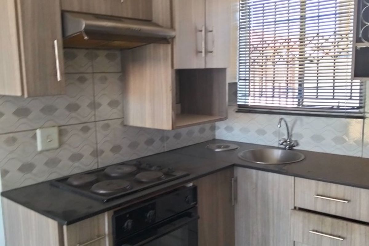Compact kitchen featuring modern laminate cabinetry, built-in oven with electric hob, extractor fan, and a stainless steel sink with tiled backsplash.