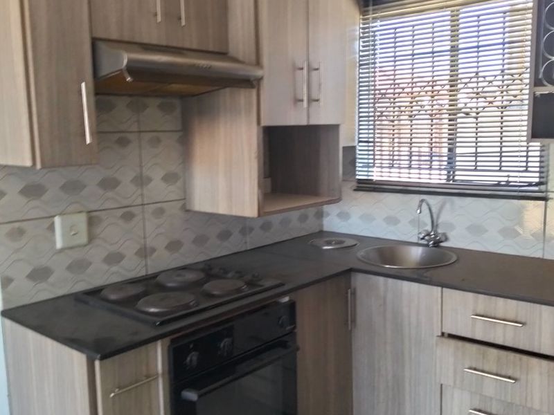 Compact kitchen featuring modern laminate cabinetry, built-in oven with electric hob, extractor fan, and a stainless steel sink with tiled backsplash.