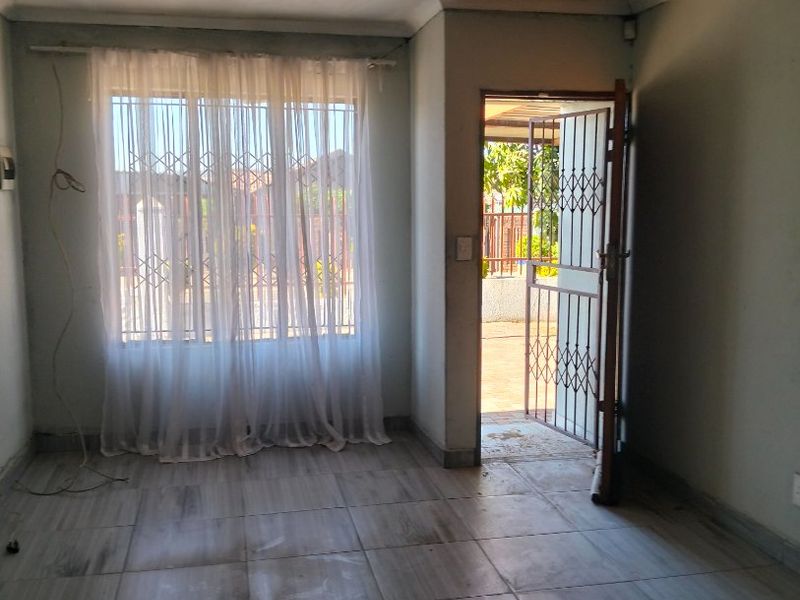 An empty living room featuring tiled flooring, security gate access, and window security bars, requiring cosmetic updates to the ceiling and walls.