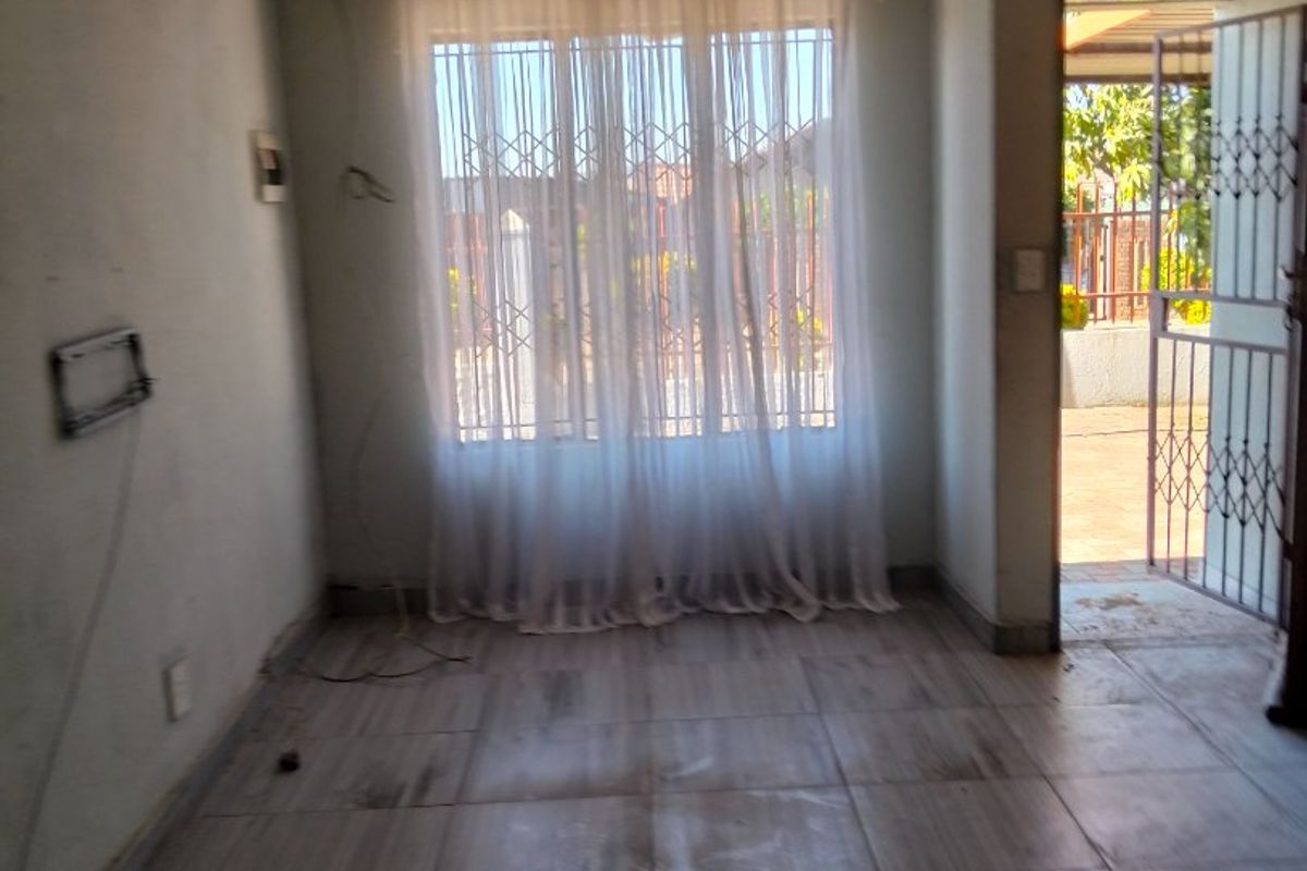 An empty living room featuring tiled flooring, security bars on the window, and a security gate leading to the exterior.