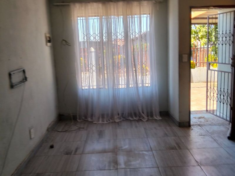 An empty living room featuring tiled flooring, security bars on the window, and a security gate leading to the exterior.