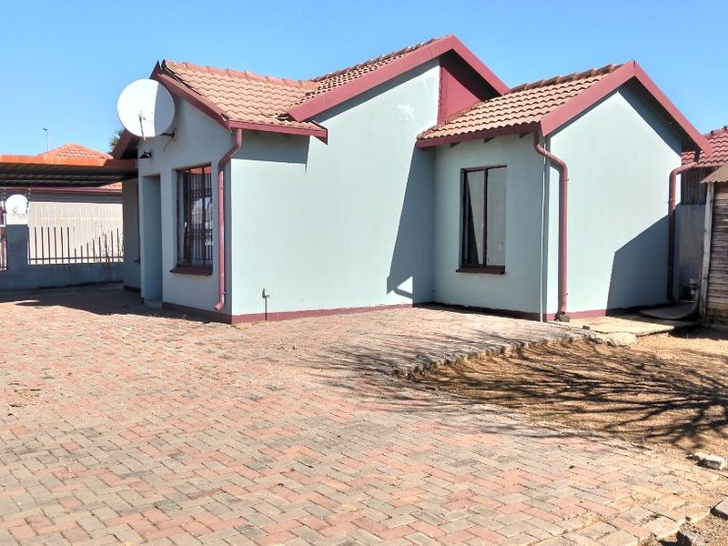 Front view of a single-story house featuring a tiled roof, paved driveway, and security bars on the windows.