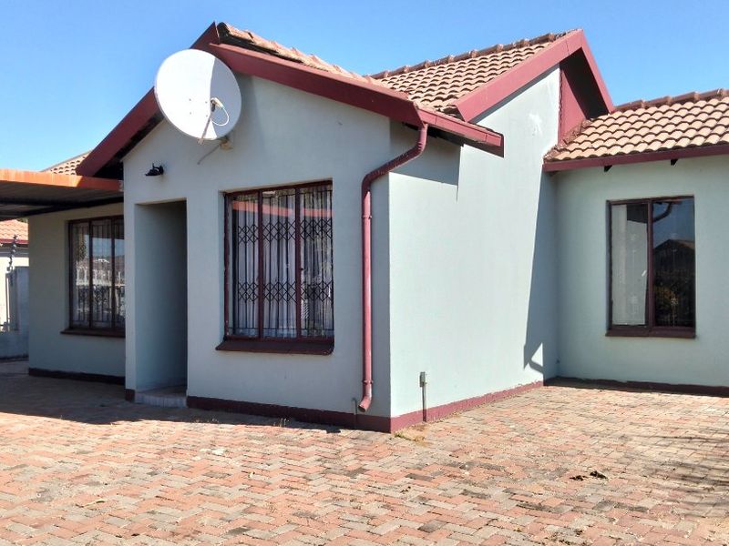 Front elevation of a single-story house featuring a tiled roof, brick-paved driveway, and security bars on the windows.
