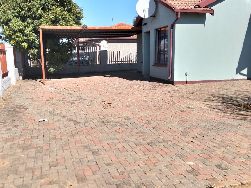 Front exterior view of the property featuring a paved driveway, a covered carport, and a tiled roof structure.