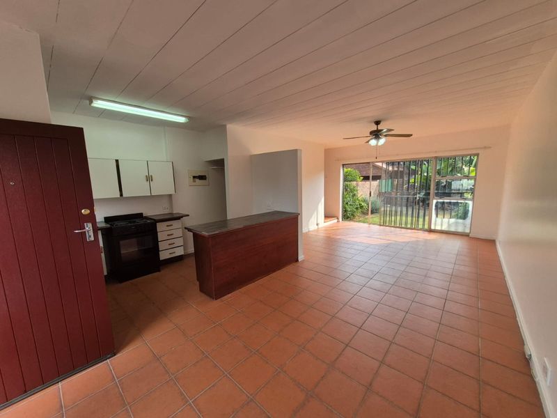 Open-plan living and kitchen area featuring tiled floors, a breakfast bar, and direct access to the rear garden through a sliding glass door.