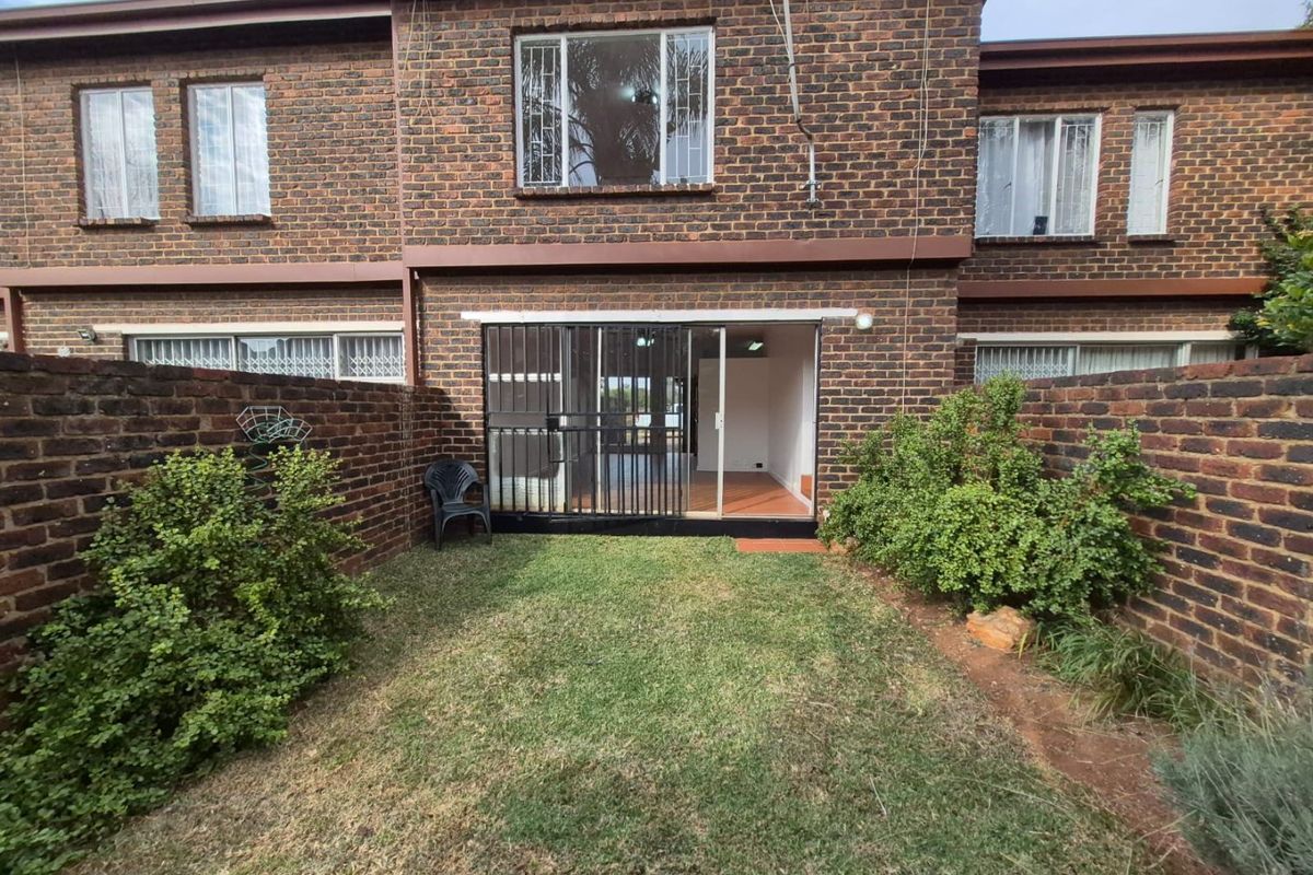 Rear view of a townhouse featuring a private garden with a lawn, enclosed by brick boundary walls and accessible via a sliding glass door.