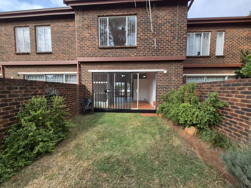 Rear view of a townhouse featuring a private garden with a lawn, enclosed by brick boundary walls and accessible via a sliding glass door.
