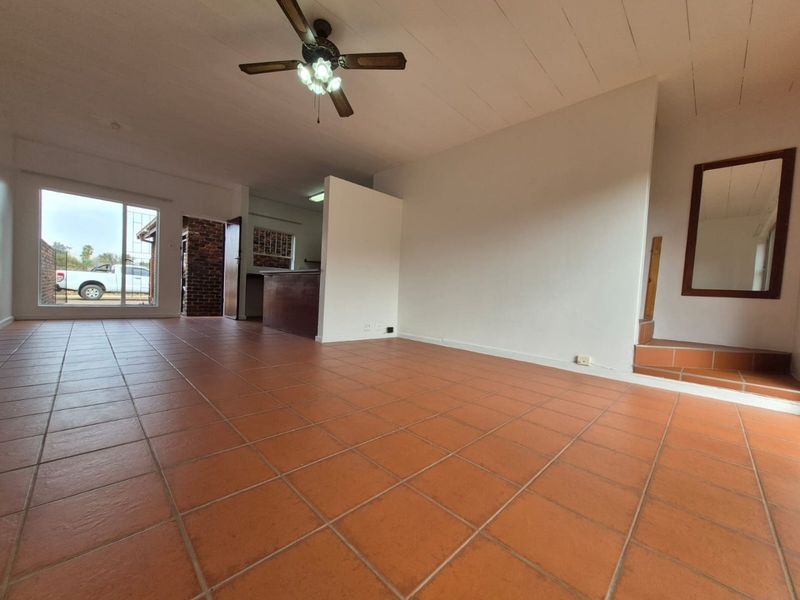 Spacious open-plan living area featuring terracotta floor tiles, a ceiling fan, and a built-in breakfast bar, offering a versatile layout for modern living.