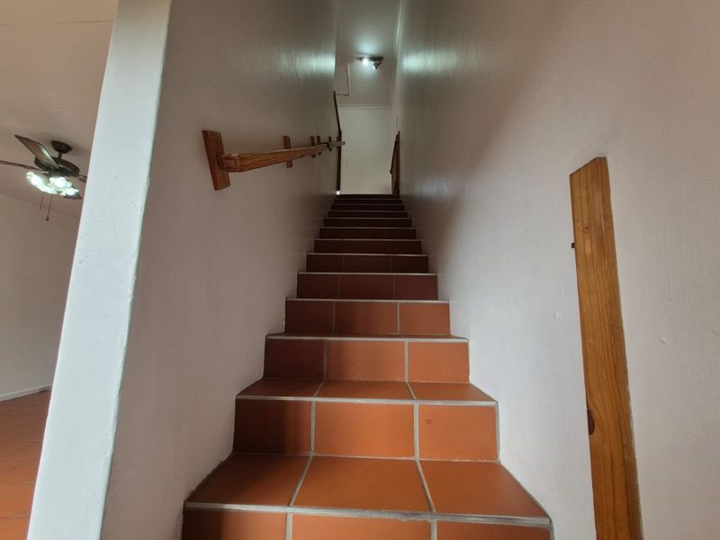 A functional staircase featuring terracotta-style floor tiles and a simple wooden handrail, leading to the upper level of the townhouse.