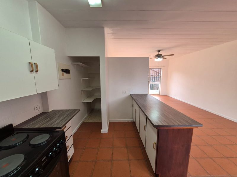 Open plan kitchen and living area featuring tiled floors, built-in cabinetry, laminate countertops, and a ceiling fan in a neutral, vacant space.