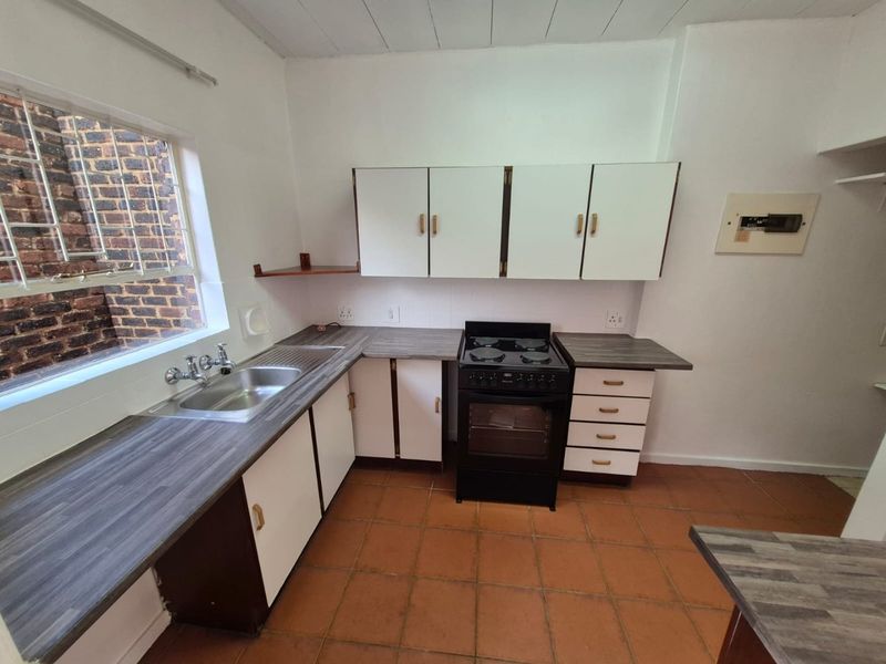 A functional kitchen featuring laminate countertops, a stainless steel sink, a freestanding electric stove, and ample built-in cabinetry with tiled flooring.