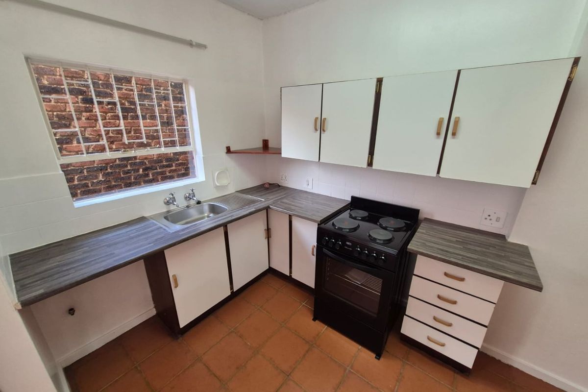 A functional kitchen featuring laminate countertops, built-in cabinetry, a stainless steel sink, and a freestanding electric stove with tiled flooring.