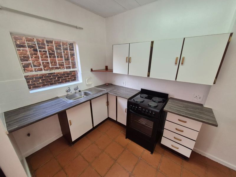 A functional kitchen featuring laminate countertops, built-in cabinetry, a stainless steel sink, and a freestanding electric stove with tiled flooring.