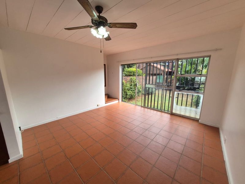 Spacious living area featuring terracotta floor tiles, a ceiling fan, and large sliding glass doors providing direct access to the rear garden.
