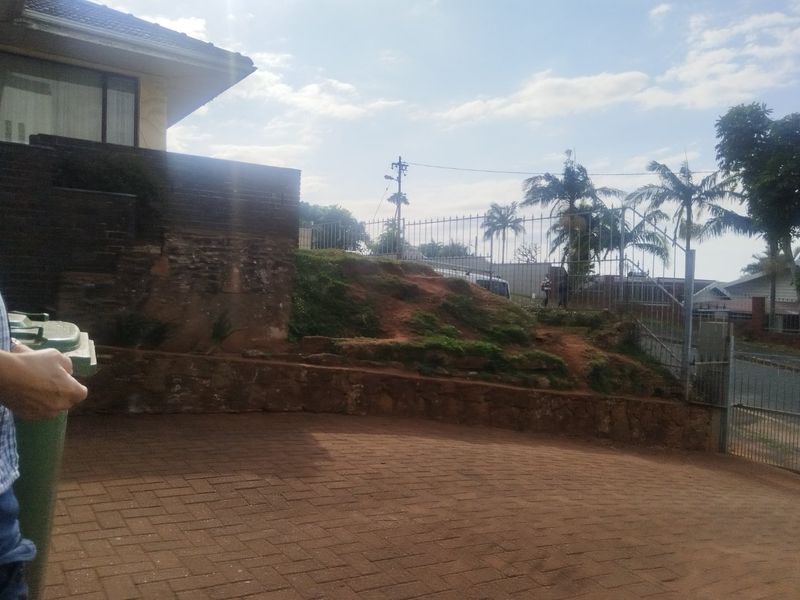 Front exterior view showing a paved driveway, retaining wall, and metal fencing with an eroded soil embankment area.