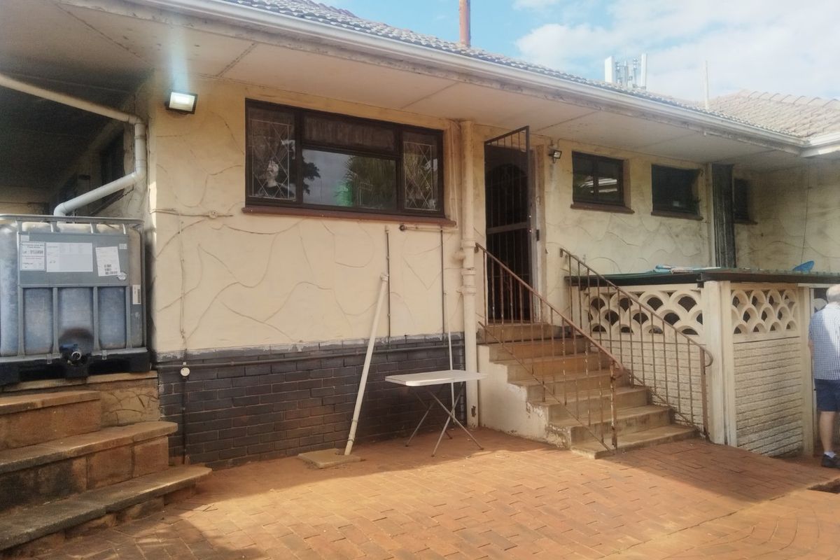 Rear exterior view of the property featuring a paved patio area, concrete stairs with metal railings, and a textured rendered facade with brick base.