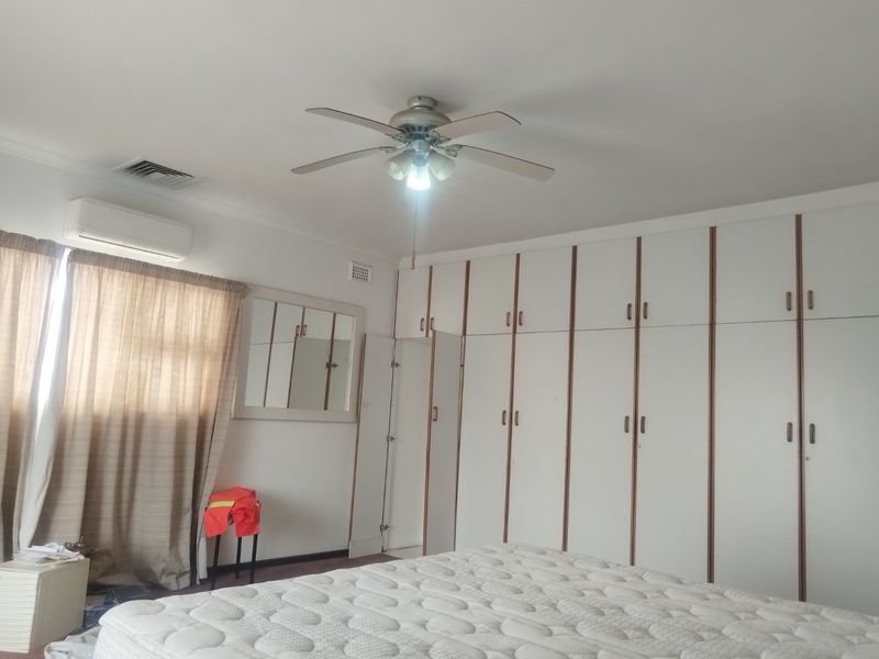 Spacious bedroom featuring extensive built-in cabinetry, a ceiling fan, and a wall-mounted air conditioning unit.