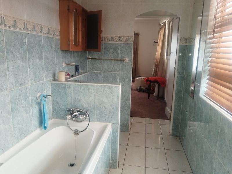 A dated bathroom featuring a built-in bathtub with wall-mounted mixer, tiled walls, and tiled flooring, offering potential for a modern renovation.
