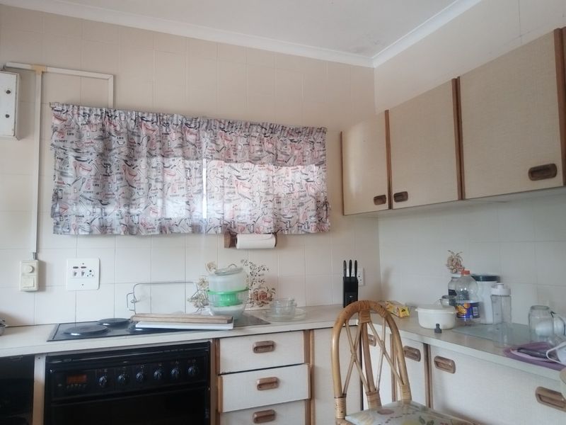 A functional kitchen featuring dated cabinetry, a built-in oven with electric hob, and tiled backsplash, offering potential for a modern renovation.