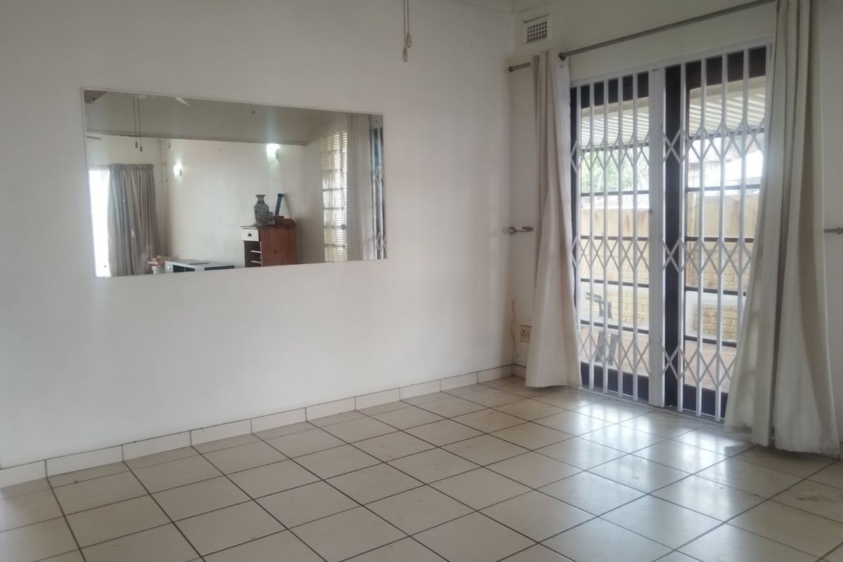 An empty living room featuring tiled flooring, a ceiling fan, and a sliding glass door with a security gate leading to the exterior.