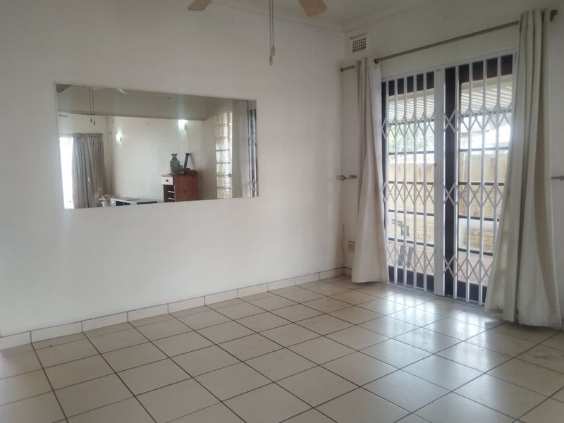 An empty living room featuring tiled flooring, a ceiling fan, and a sliding glass door with a security gate leading to the exterior.