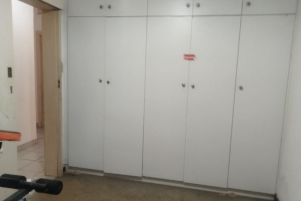 A bedroom featuring extensive built-in white cabinetry, providing ample storage space. The room requires flooring updates and general maintenance.