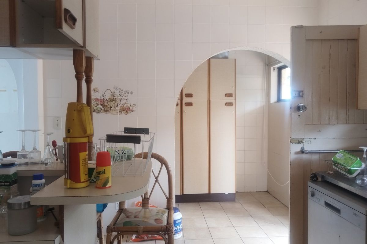 A dated kitchen featuring tiled walls, built-in cabinetry, and a breakfast counter, connected to an adjacent space via a classic archway.