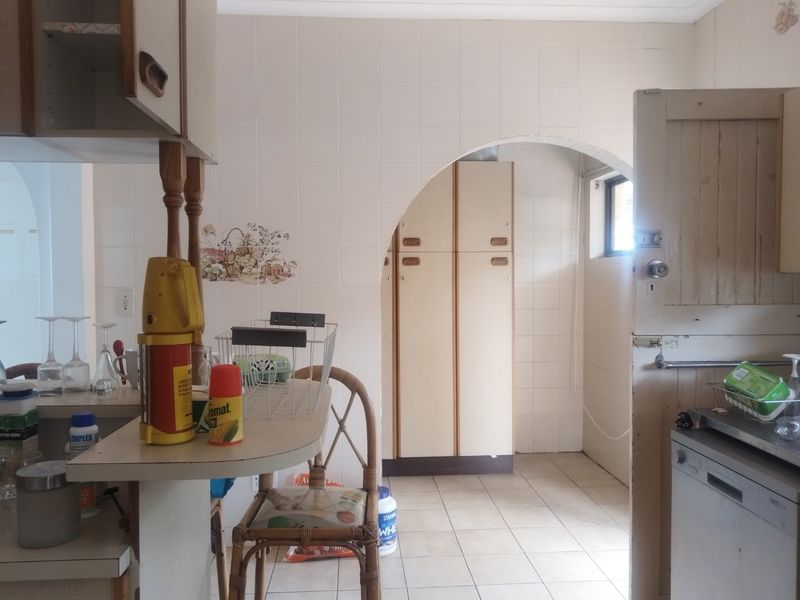 A dated kitchen featuring tiled walls, built-in cabinetry, and a breakfast counter, connected to an adjacent space via a classic archway.
