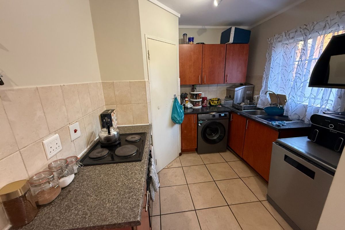 A functional kitchen featuring wood-tone cabinetry, laminate countertops, tiled backsplash, and integrated electric hob, offering a practical layout for daily meal preparation.
